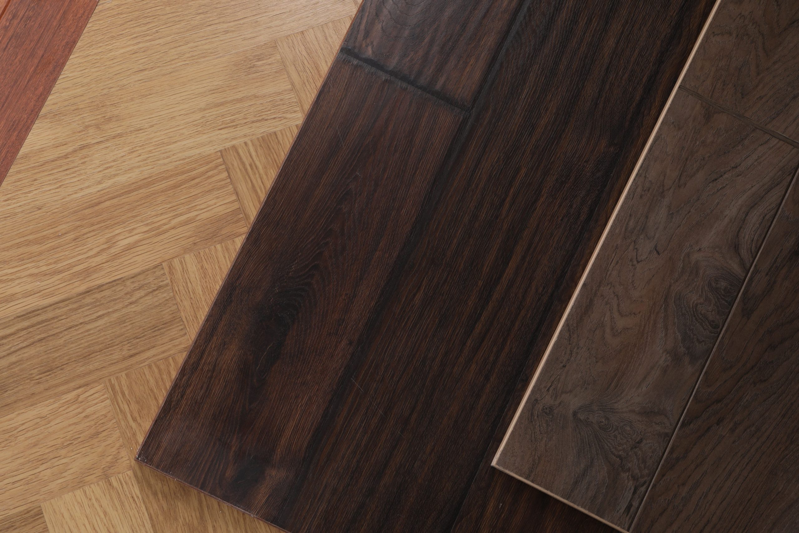 Three different wood flooring samples with varied shades and grain patterns laid out on a wooden surface.