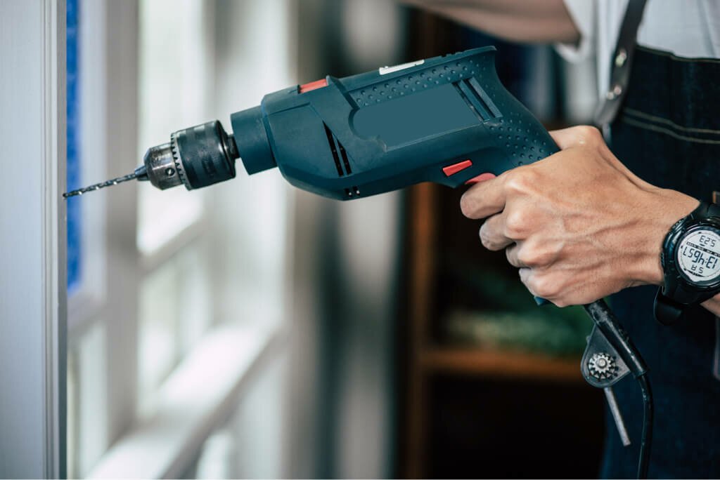 the carpenter holds the drill and drills the window